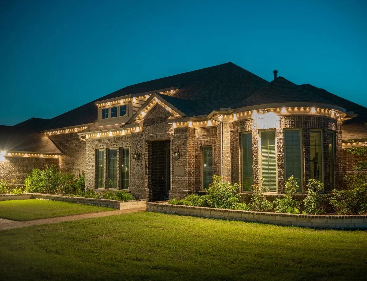 Brick home with warm white lights outlining the roofline and windows