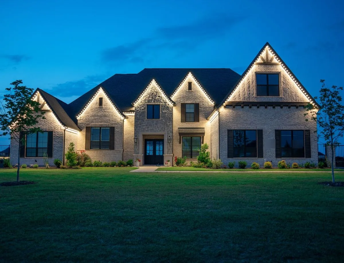 Stone home with warm white lights along every gable at dusk